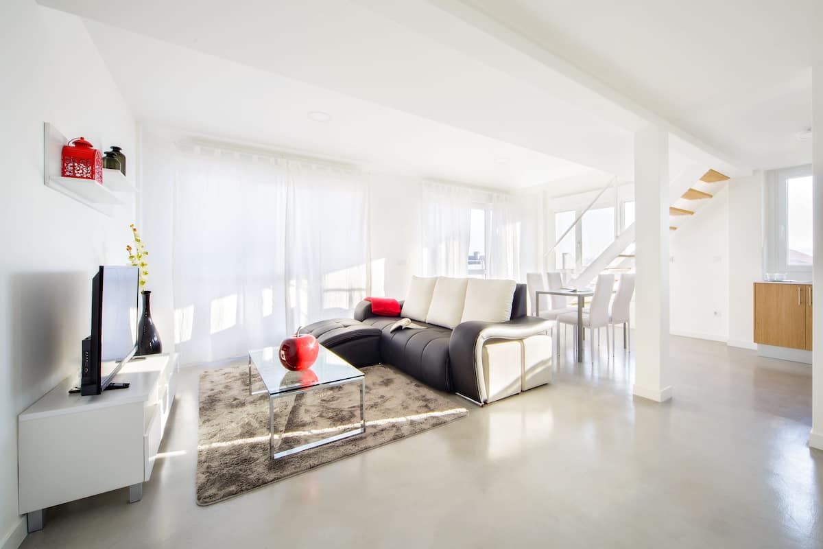 A modern living room with a sectional sofa, a glass coffee table, and a flat-screen TV on a white console.