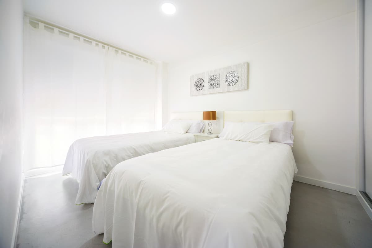 A hotel room with two beds, a large window with sheer curtains, and a wall-mounted artwork.