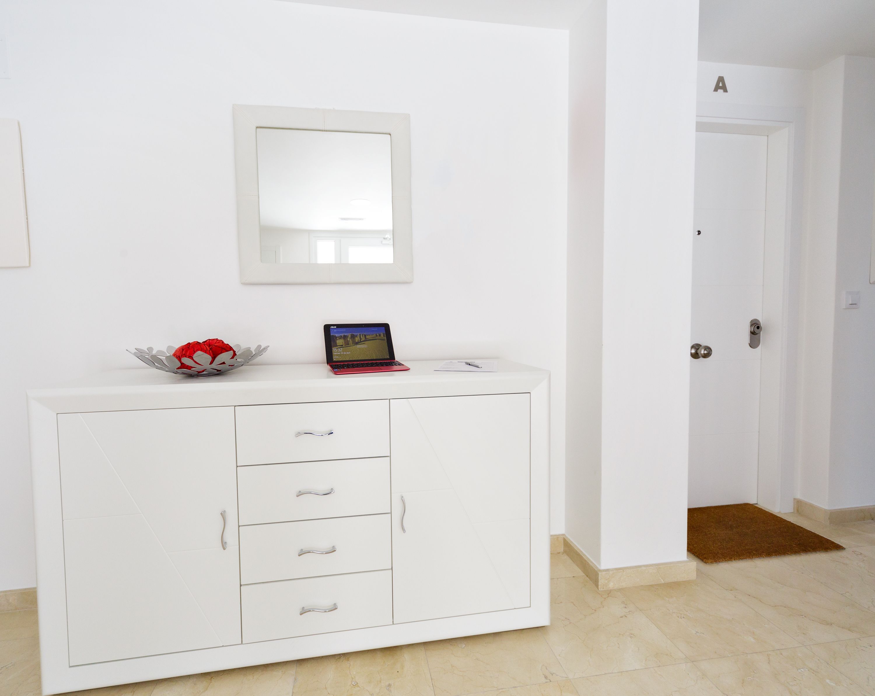 Un meuble blanc avec des tiroirs, et un ordinateur portable posé dessus.