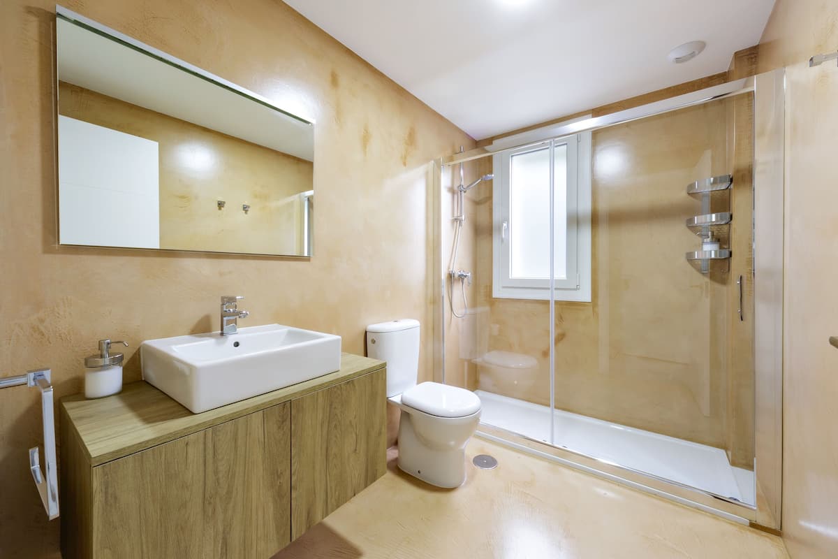 A modern bathroom with a wooden vanity, a white sink, and a glass-enclosed shower.