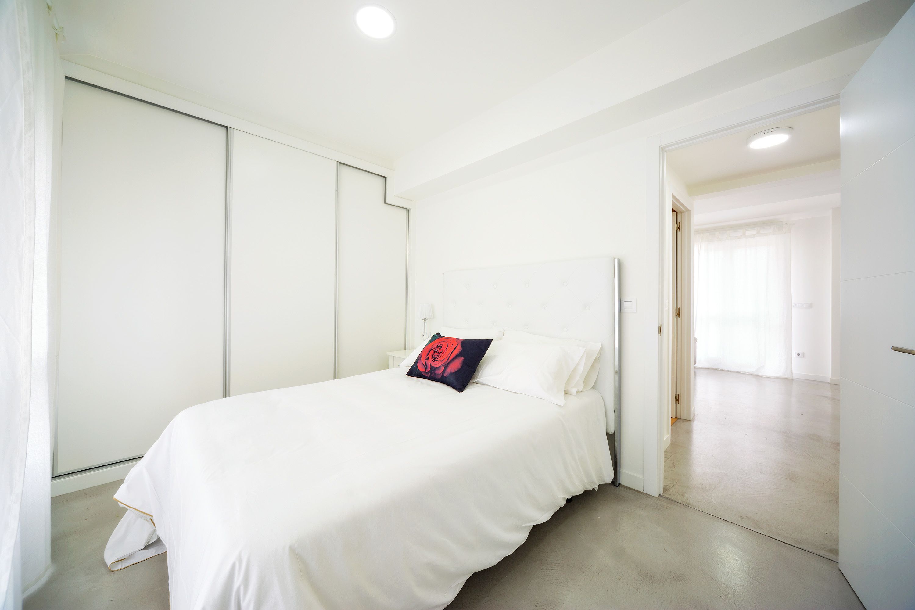 Une chambre à coucher avec un lit, des murs blancs et une porte qui donne sur une autre pièce.