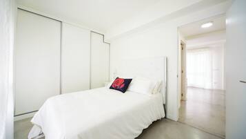 Une chambre à coucher avec un lit, des murs blancs et une porte qui donne sur une autre pièce.