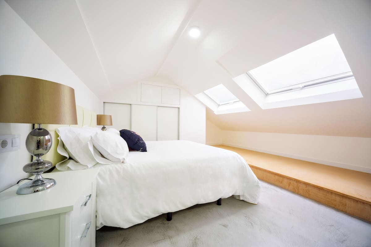 A bedroom with a bed, bedside table, lamp, and skylights.