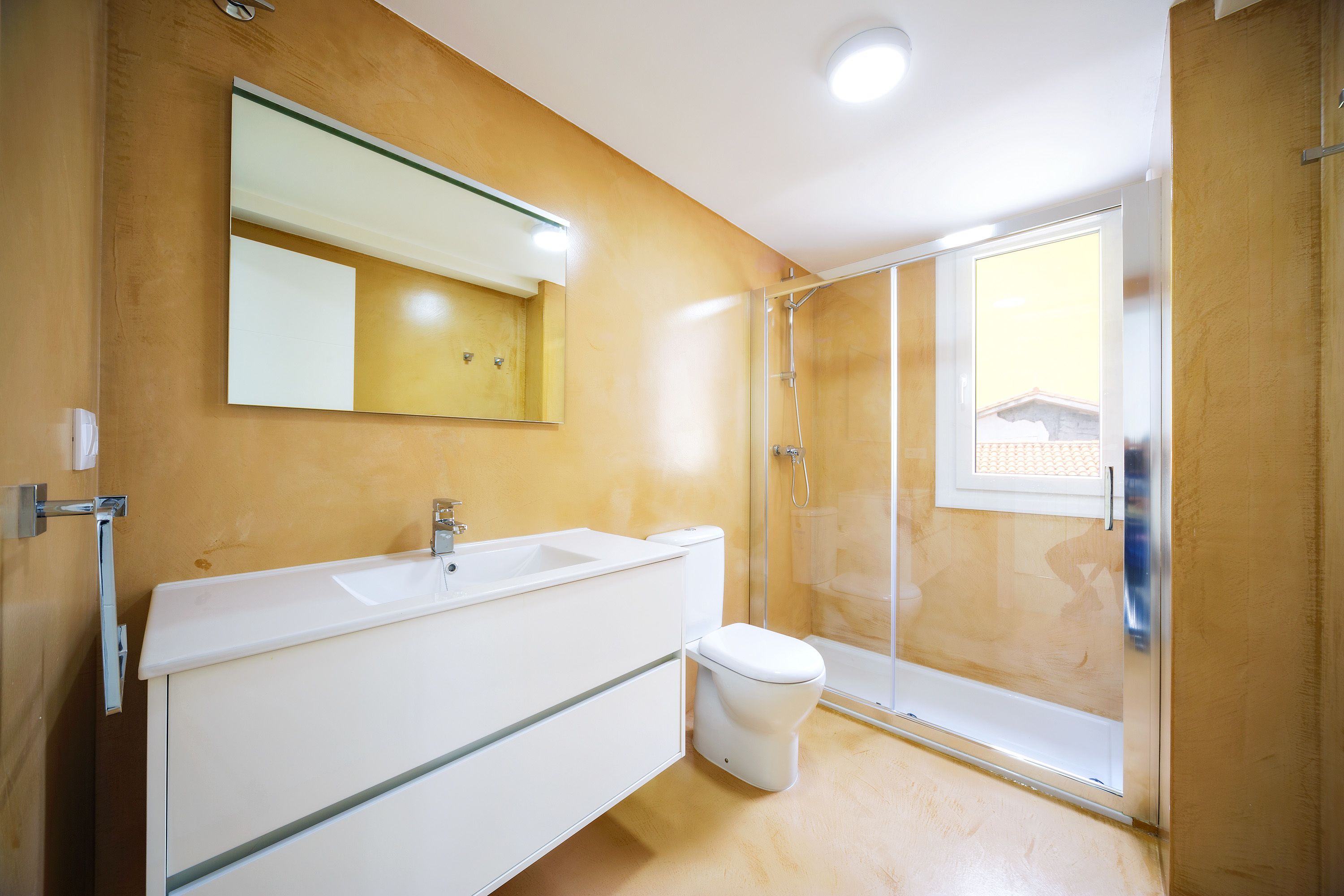 Un baño moderno con un espejo grande, un lavabo blanco y una cabina de ducha de vidrio.