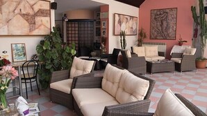 A cozy outdoor seating area with wicker furniture, potted plants, and artwork on the walls. - Hotel Ebe (Scarperia e San Piero)