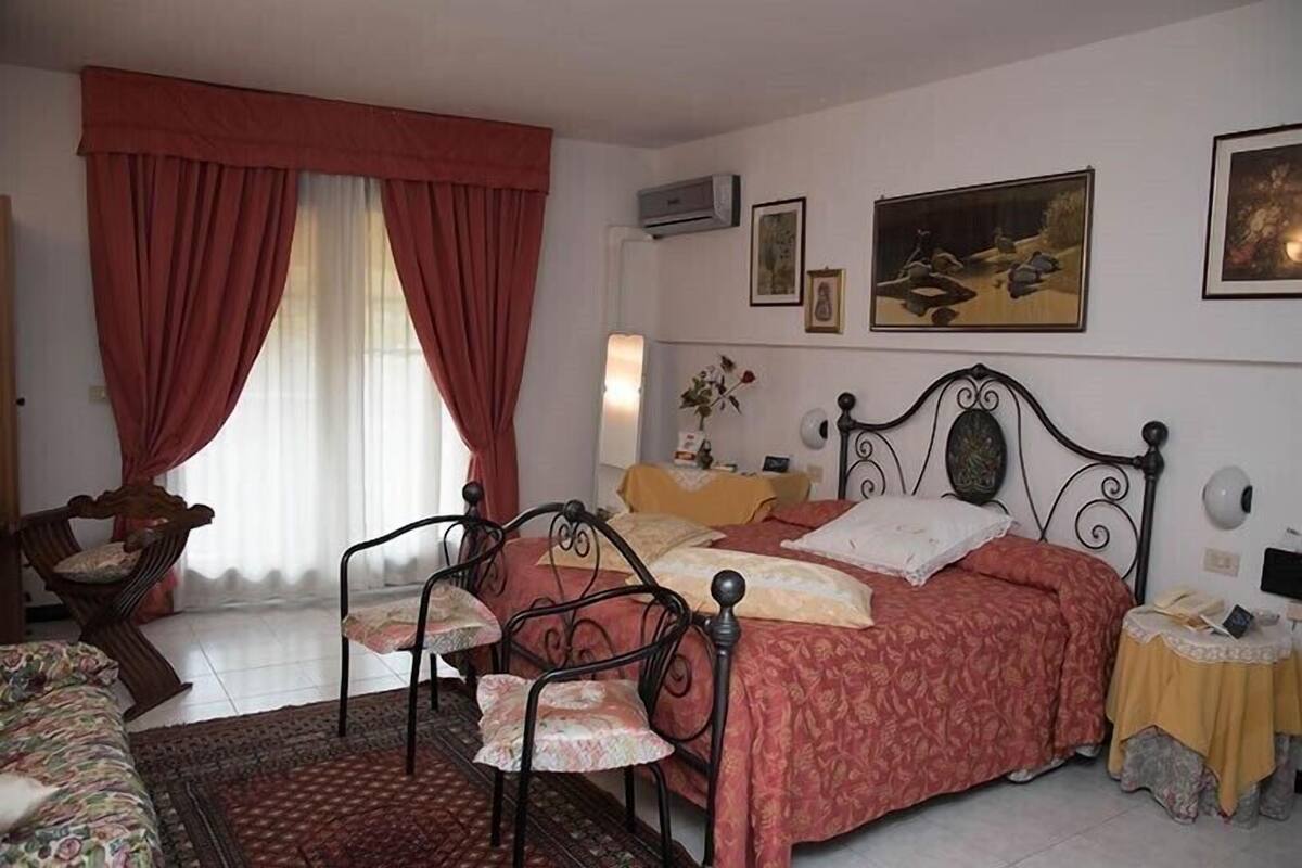 A bedroom with a bed, a chair, a table, and a window with curtains.