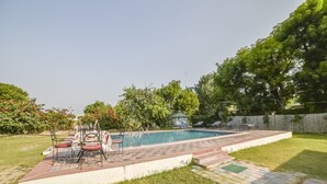 Un patio trasero con piscina, un porche con sillas y un pabellón.