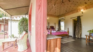 Una habitación con una cama, una mesa de madera y una silla. Hay una ventana con cortinas y una puerta que da a otra habitación.