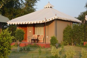 A single-story building with a large, white, tent-like roof and a red base. There are two wicker chairs on the front porch. - Lohana Village Resort (Pushkar)