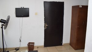 Une pièce avec une porte noire, un téléviseur fixé au mur, un ventilateur, un téléphone et un meuble.