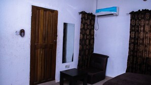 Une petite pièce avec une porte en bois, une petite table, une chaise, un lit et un appareil de climatisation fixé au mur.
