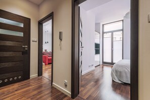 A hallway with a wooden door, a phone, and a bed in the adjacent room.