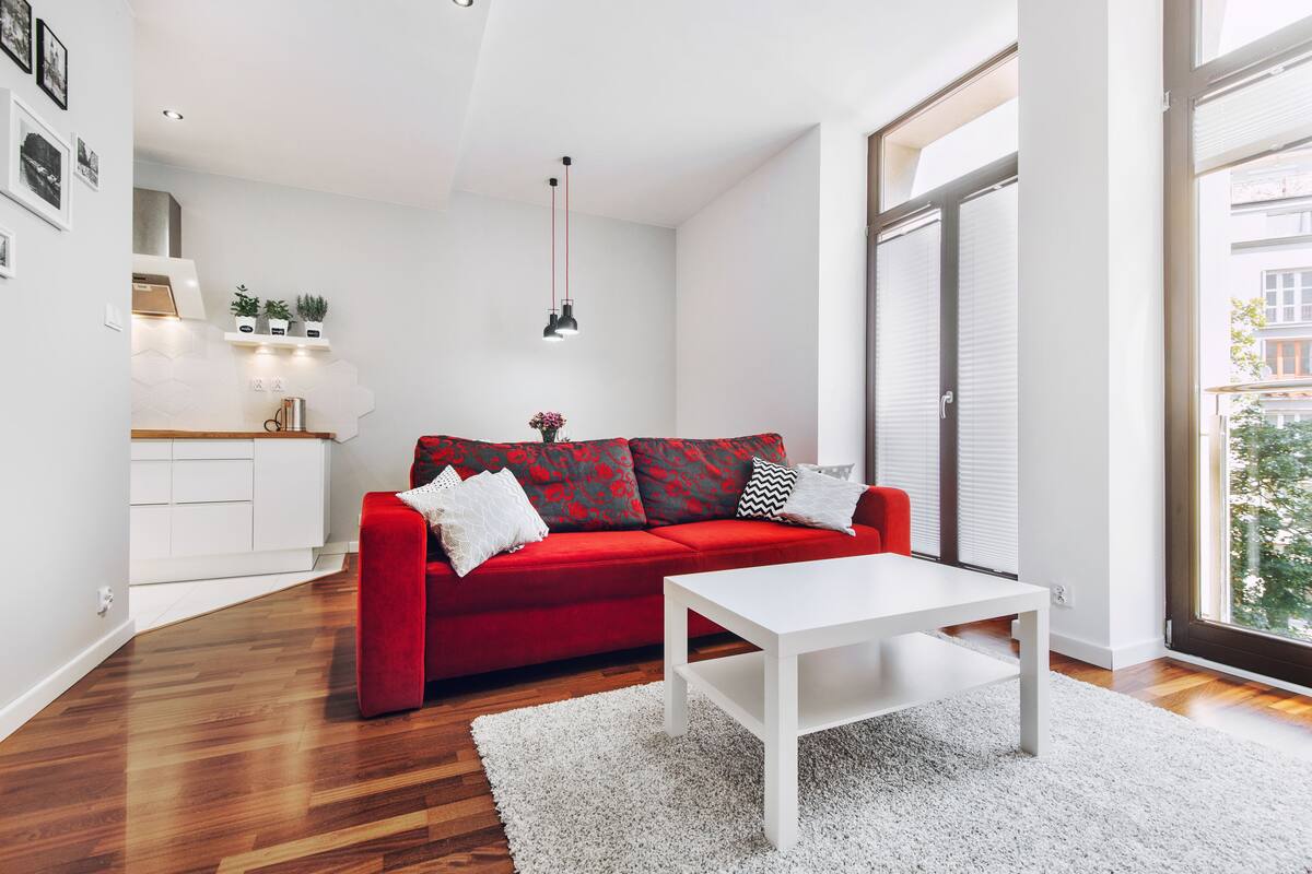 Un salon moderne avec un canapé rouge, une table basse blanche et une grande fenêtre donnant sur la ville.