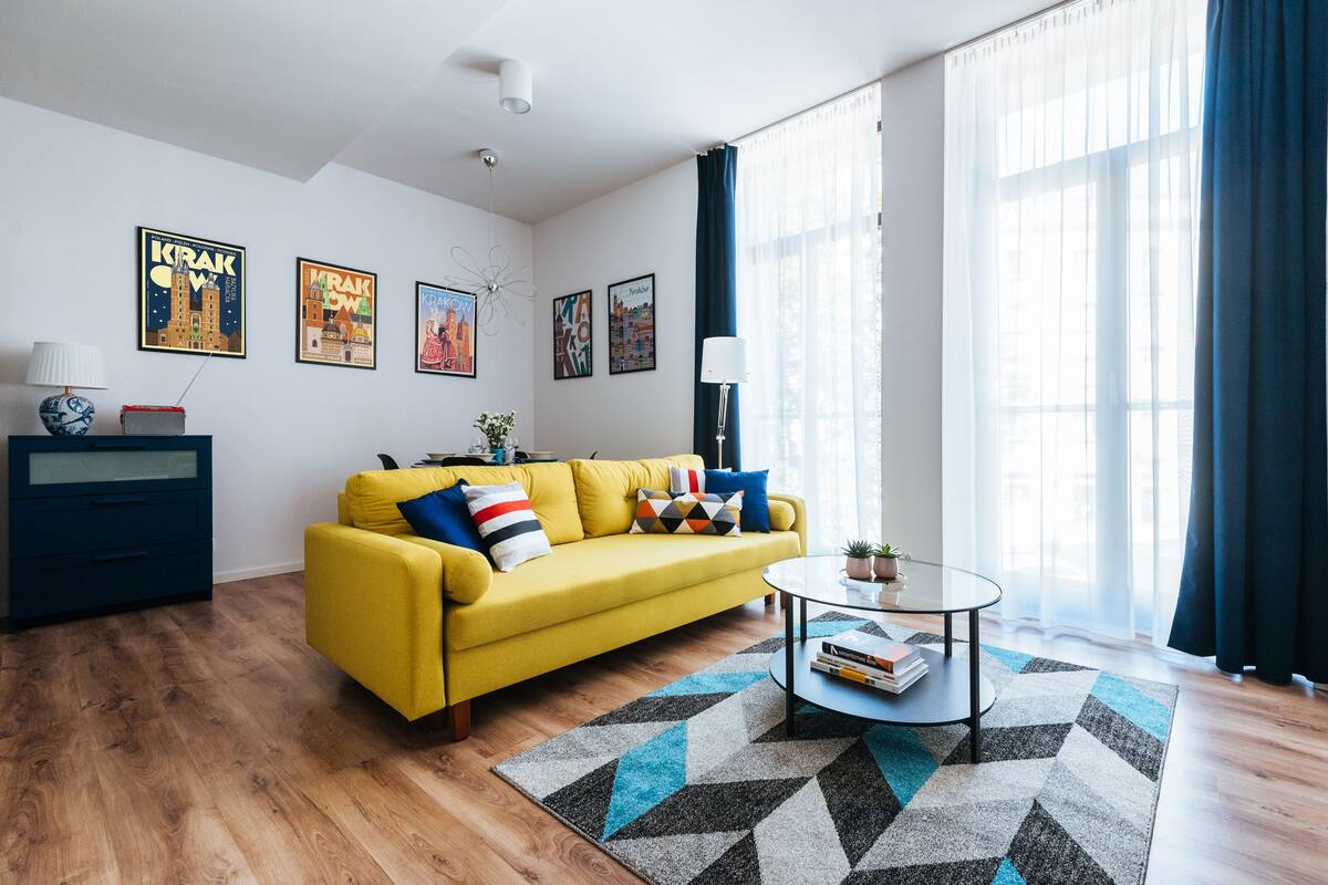 Un salon moderne avec un canapé jaune, une table basse en verre et un tapis à motifs géométriques.