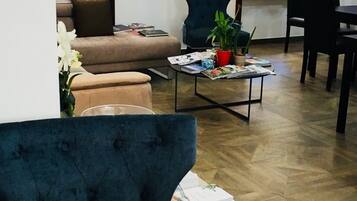 A living room with a sofa, a coffee table with magazines, a blue armchair, and a dining area with chairs.