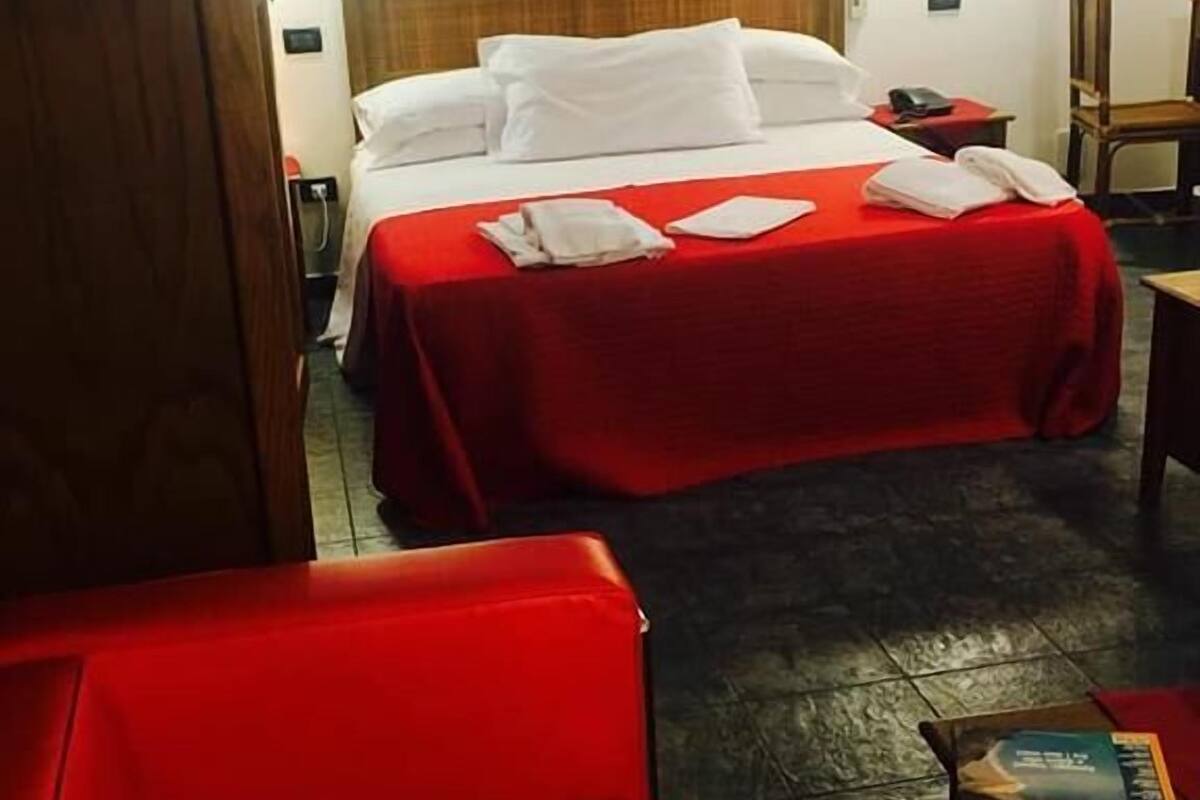 A hotel room with a bed, a red chair, a small table with a magazine, and a wooden headboard.