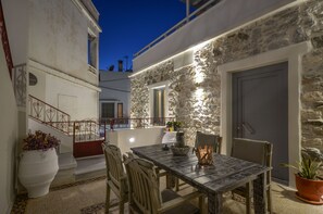 A stone-walled outdoor dining area with a table and chairs, a potted plant, and a staircase leading to an upper level. - Naxos Center Houses (Naxos)