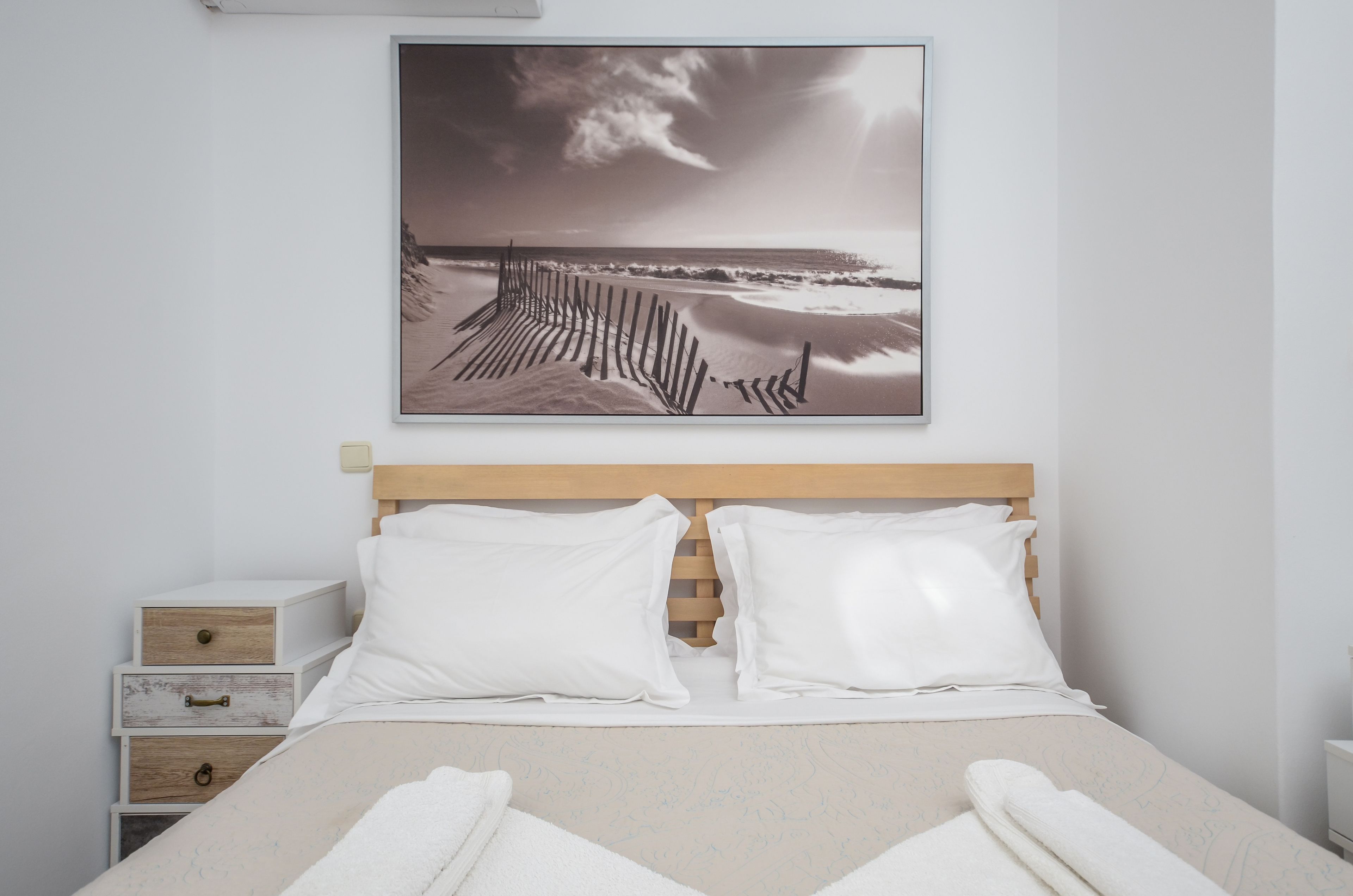 Ein Schlafzimmer mit einem hölzernen Kopfteil, weißer Bettwäsche und einem Gemälde mit einer Strandansicht an der Wand.