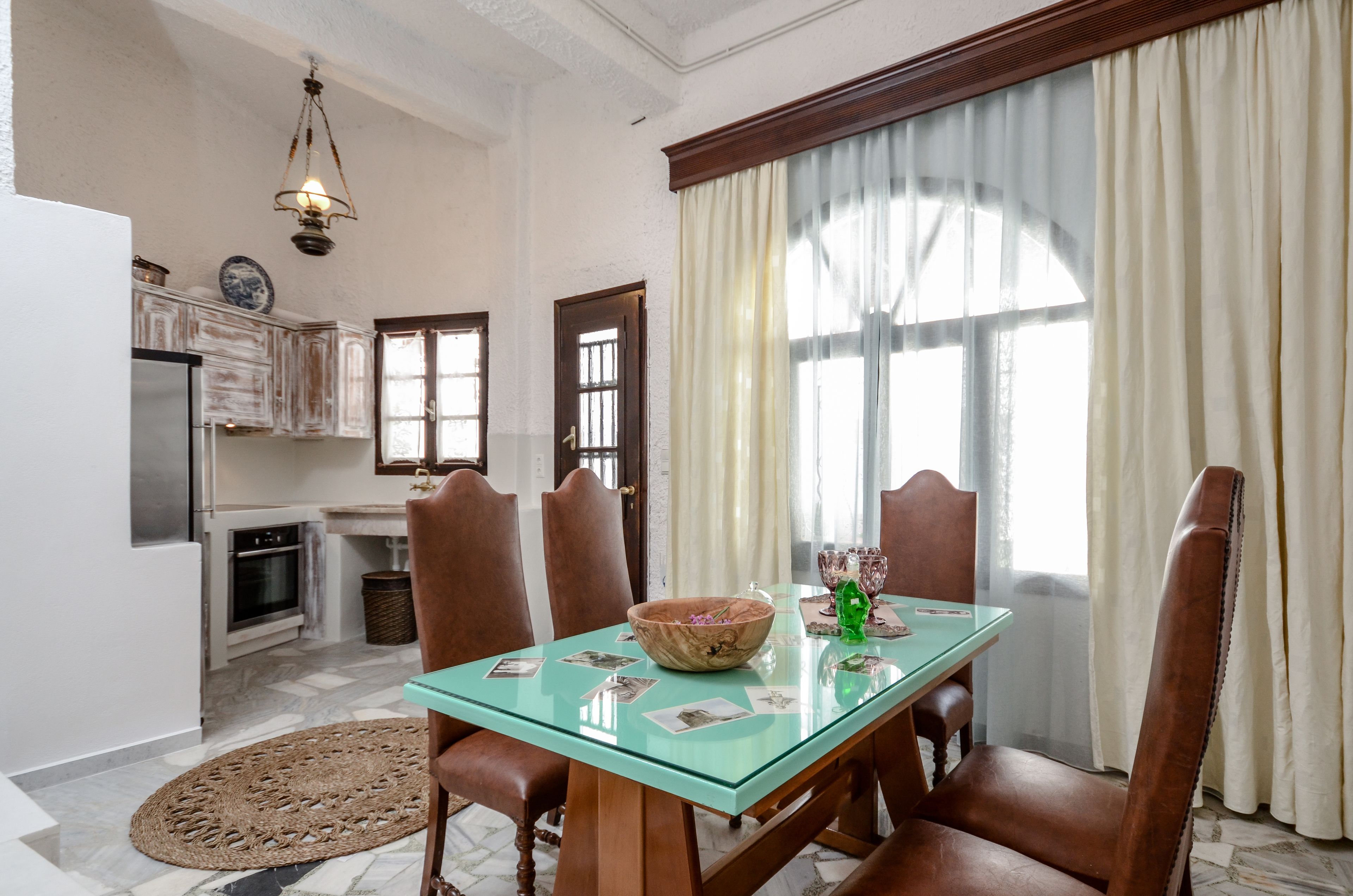A dining area with a glass table, wooden chairs, and a large window with curtains.