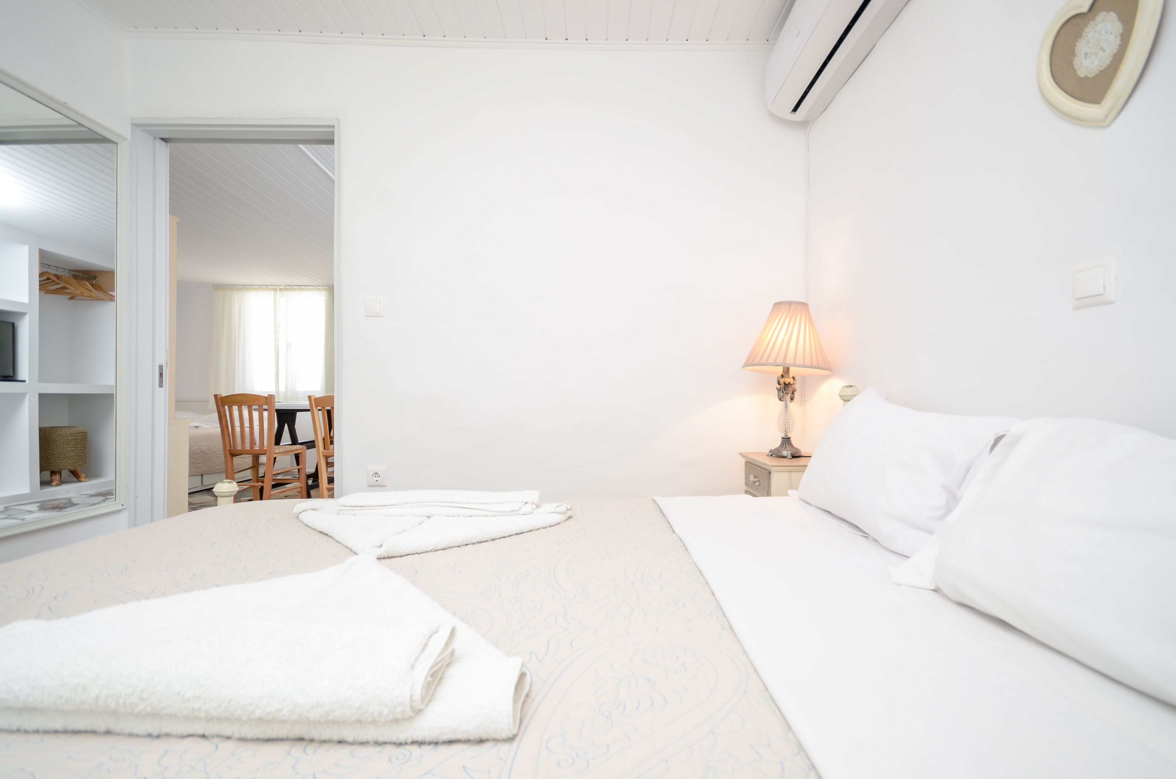 A white bedroom with a bed, a bedside table with a lamp, and a chair.