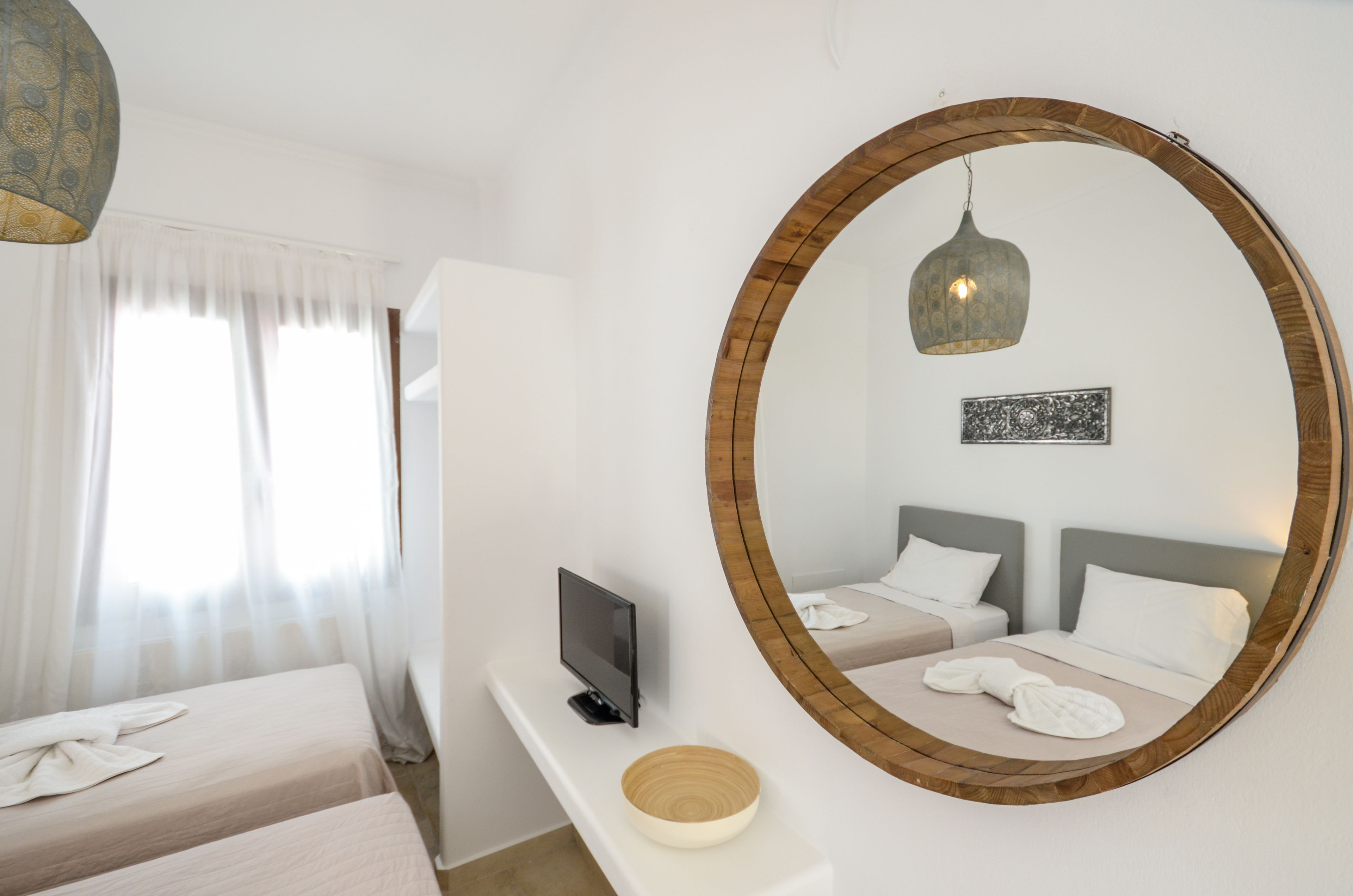 A hotel room with two beds, a TV, a mirror, and a wooden-framed mirror.
