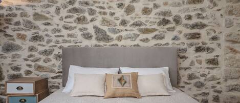 A bed with a stone wall background, a wooden nightstand with drawers, and a single decorative pillow.