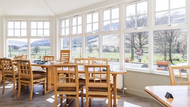 Comedor con muebles de madera y ventanas amplias que ofrecen vistas a un paisaje rural.