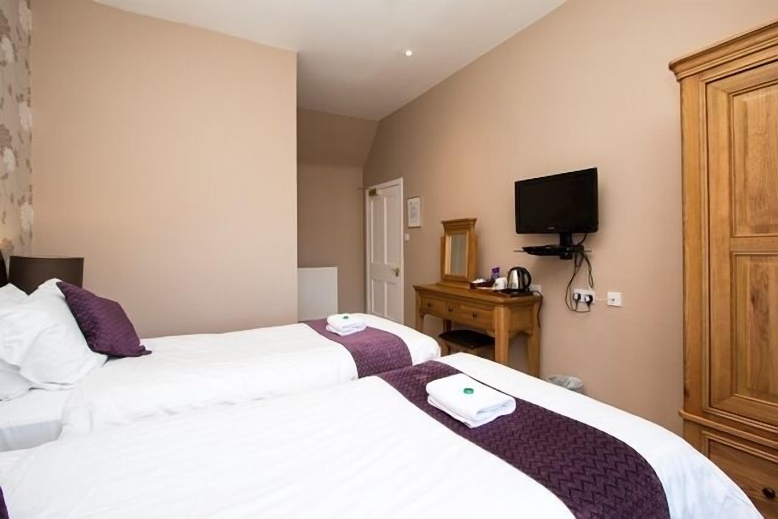 A hotel room with two beds, a wooden dresser, a television, and a wardrobe.