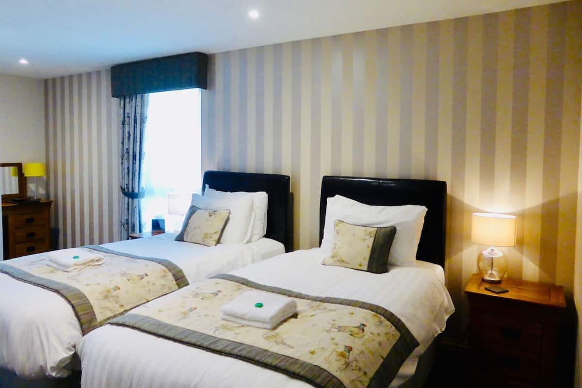Habitación de hotel con dos camas, cortinas a rayas, una lámpara de noche y una mesita de madera.