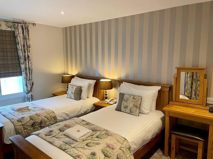 A hotel room with two beds, each with floral bedding and pillows, a wooden nightstand with a lamp, a telephone, and a mirror.