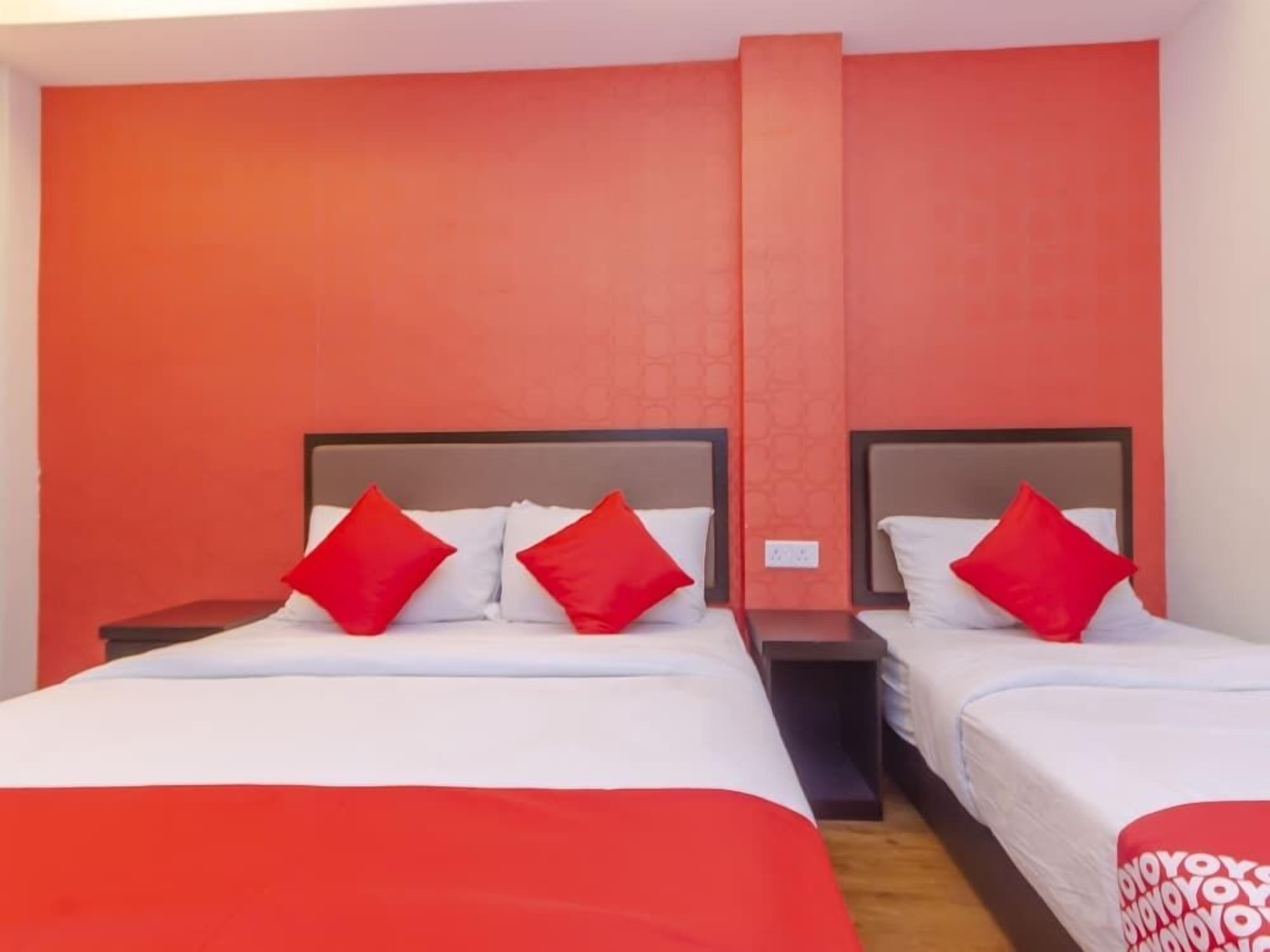 A hotel room with two beds, each with a red pillow, white bedding, and a wooden nightstand.