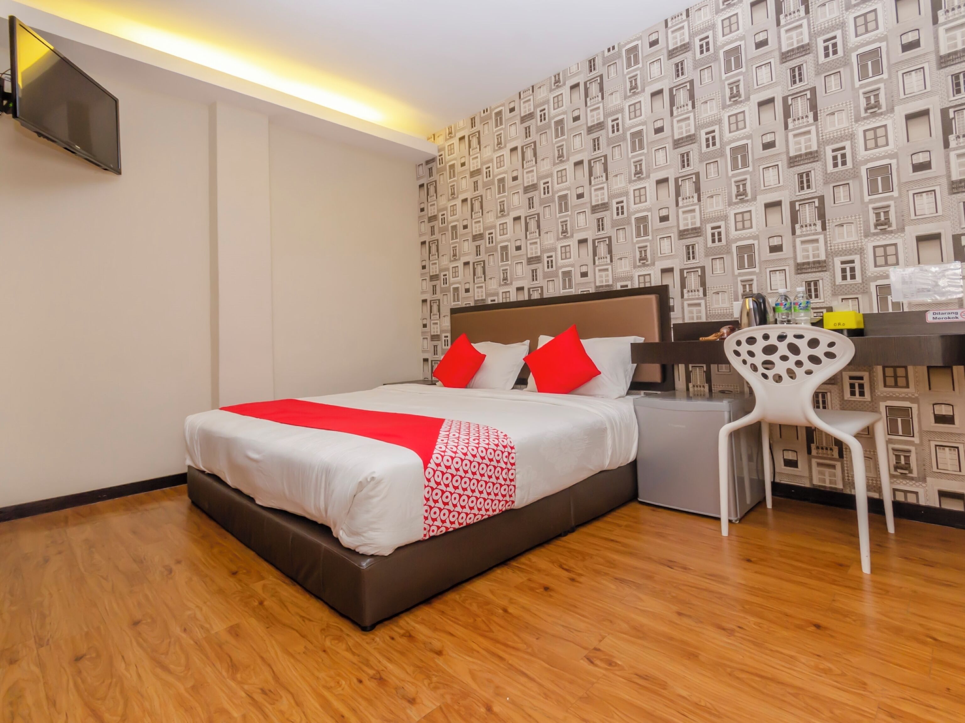 A hotel room with a bed, a desk, a chair, and a patterned wallpaper.