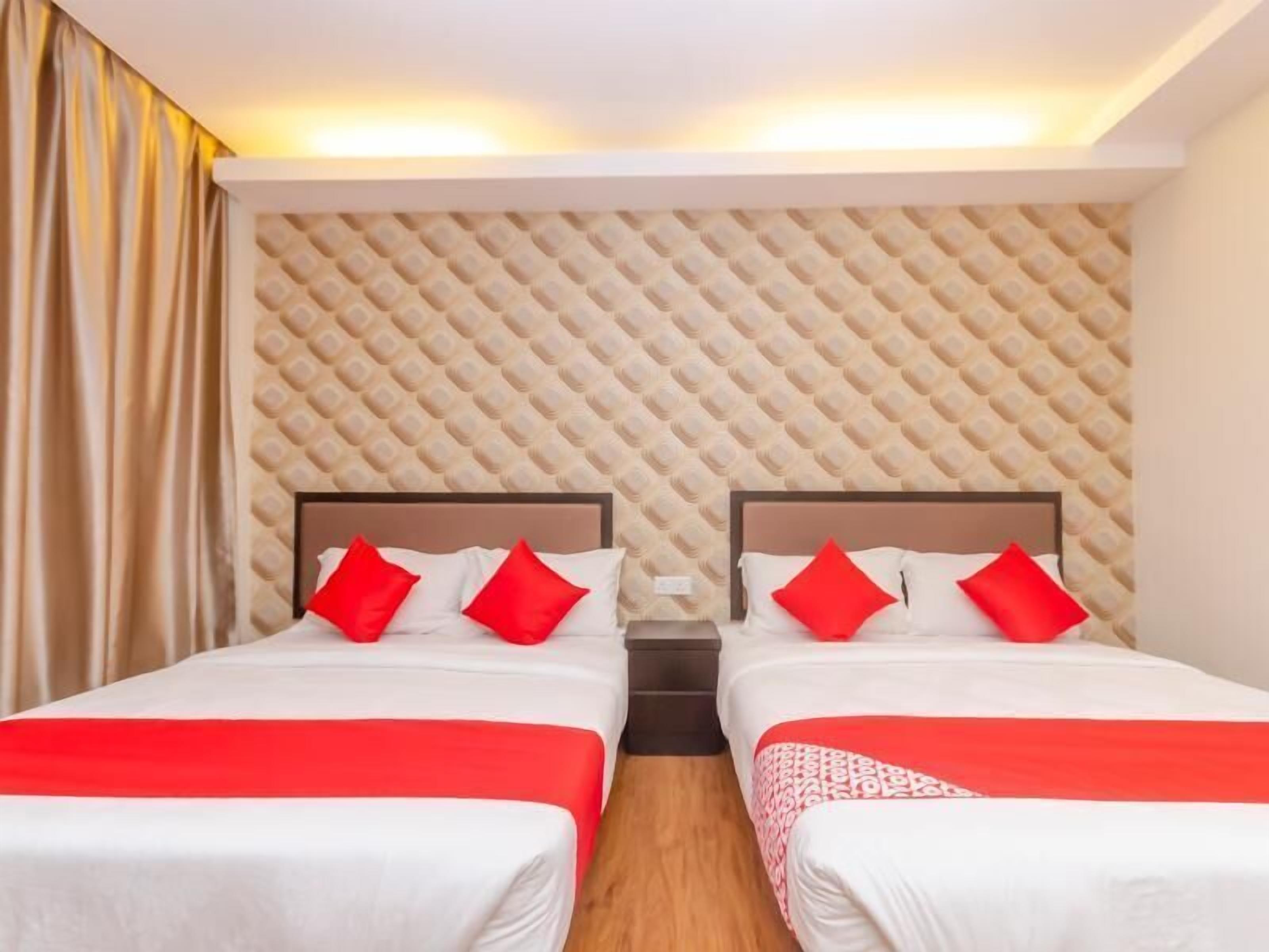 A hotel room with two beds, each with red pillows, a patterned headboard, and a red and white bedspread.