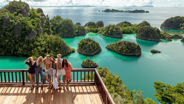 Un grupo de personas en una terraza de madera con vistas a aguas turquesas e islas exuberantes.