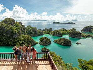 A group of people on a wooden deck overlooking turquoise waters and lush islands.