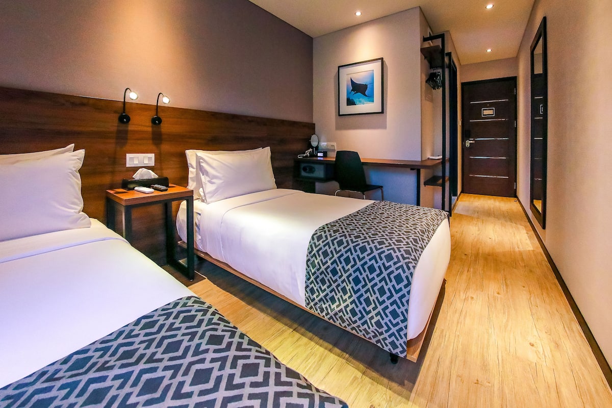 Habitación de hotel con dos camas, un escritorio, una silla y un cuadro en la pared.