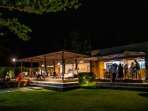 Un espace de restauration en plein air, avec des tables et des chaises, entouré d’un espace de repos abrité et d’un bar.