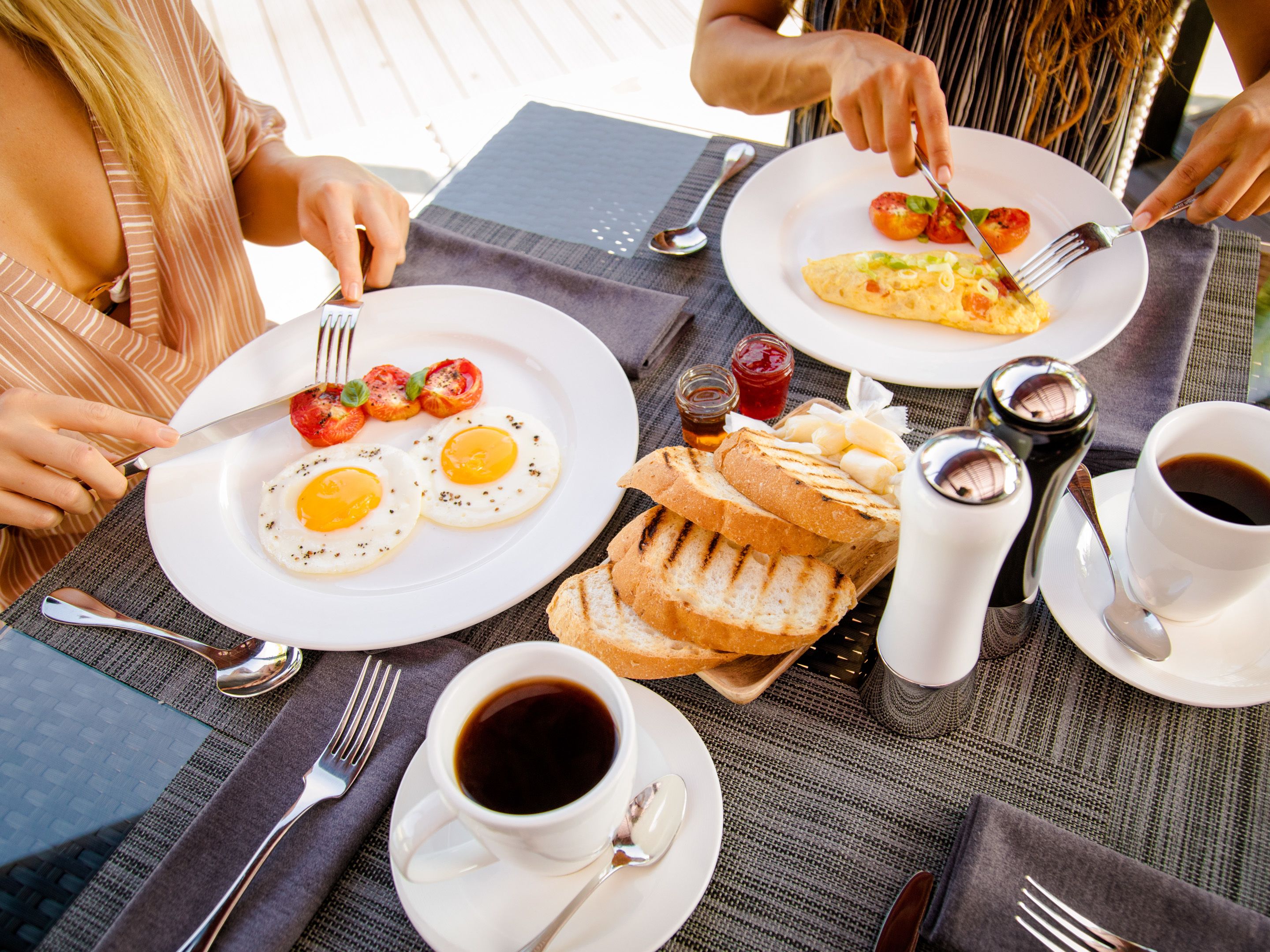 A breakfast setting with plates of eggs, toast, and tomatoes, along with cups of coffee and condiments.