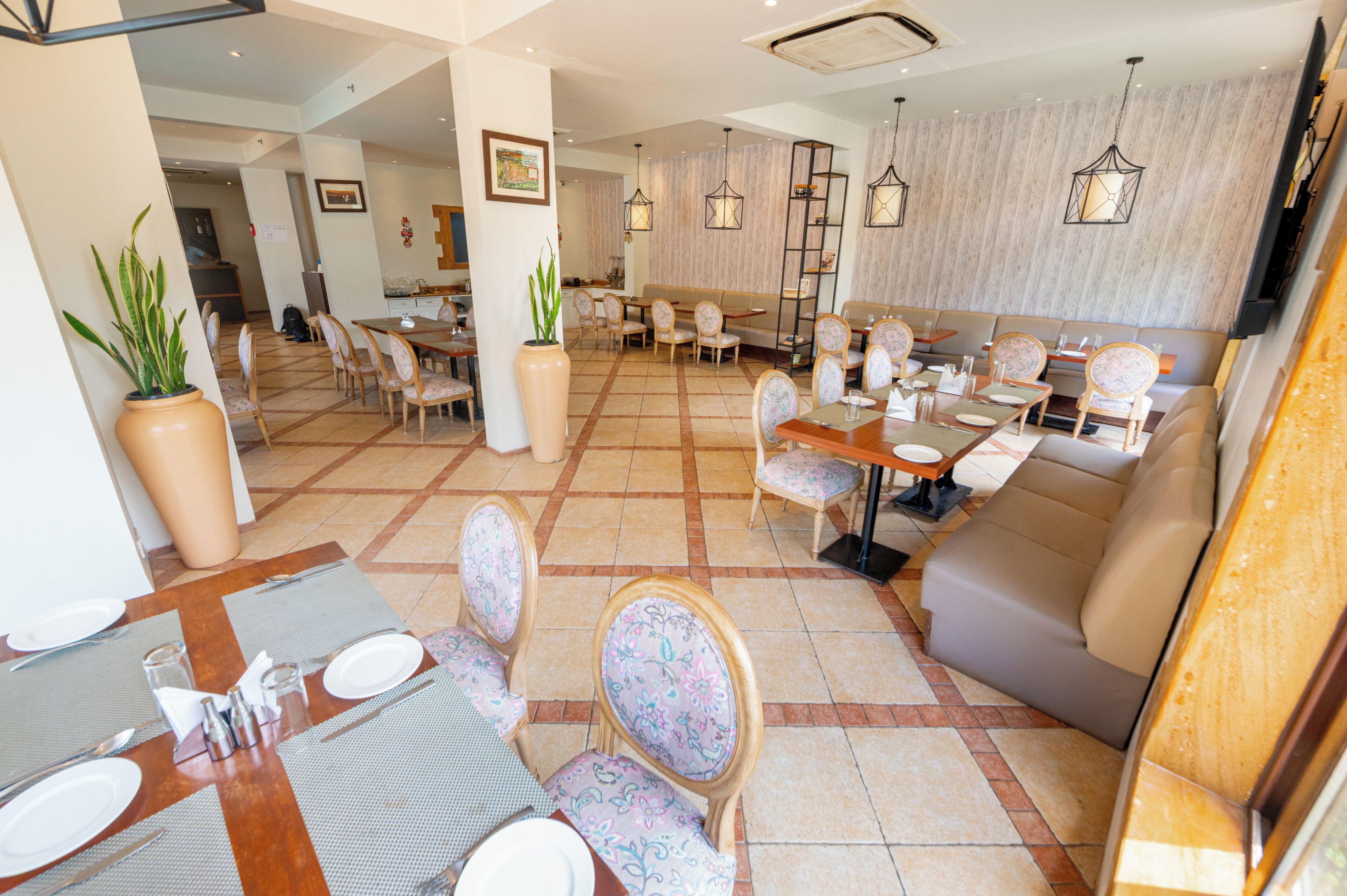 Un comedor de hotel con varias mesas y sillas, un sofá y lámparas colgantes.