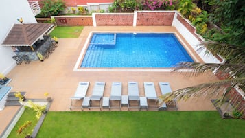 A rectangular pool with a diving board, surrounded by a brick wall and lush greenery.