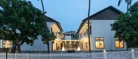 Uma casa moderna de dois andares com cerca branca, piscina e um letreiro que diz 'The Ivy Arjuna'.