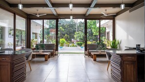 A spacious room with a large window, a ceiling fan, and a dining area with a view of a garden. - The Ivy Anjuna (Anjuna)