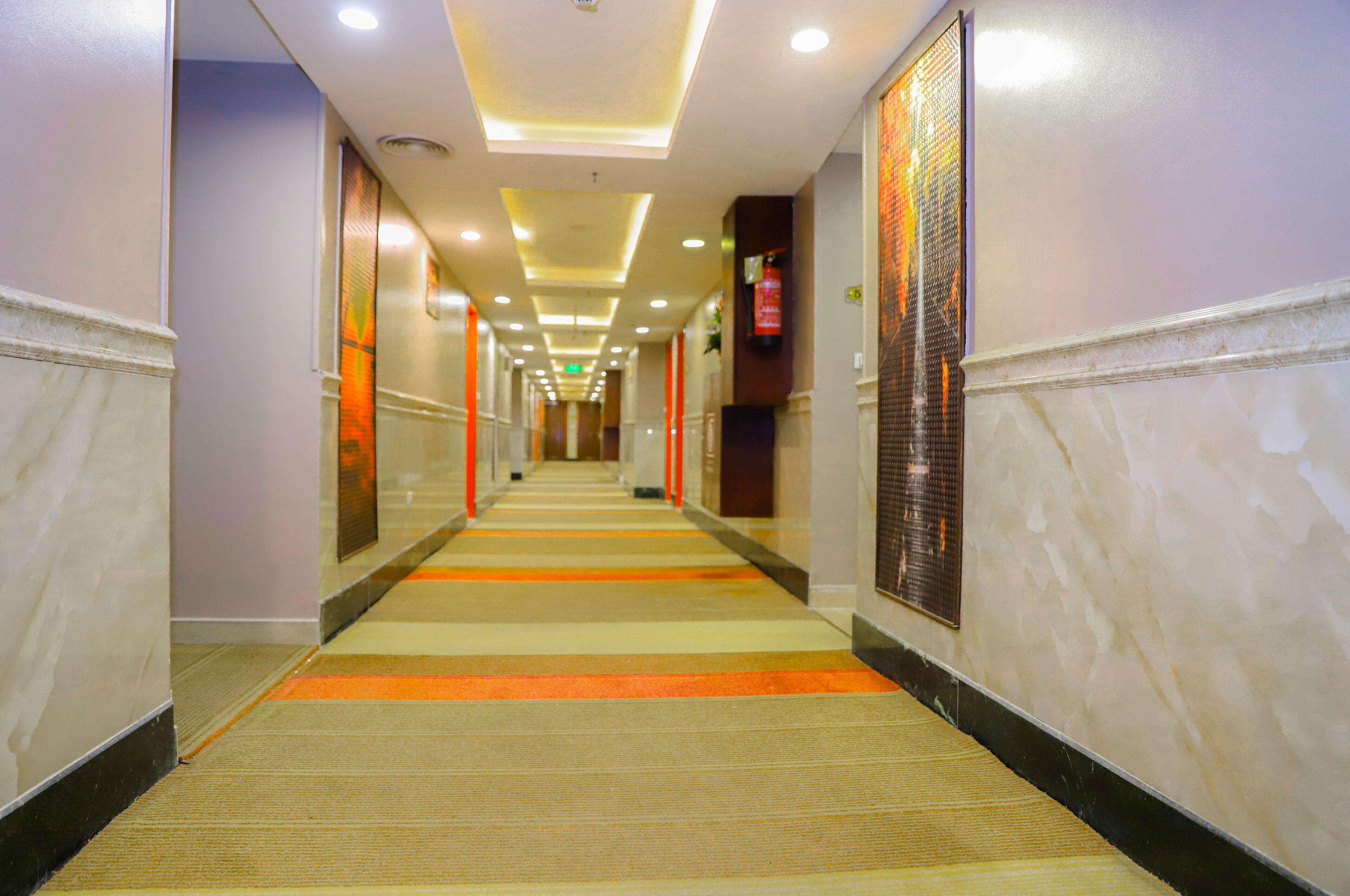 Een hotelgang met een vloerkleed, wandpanelen en inbouwverlichting in het plafond.