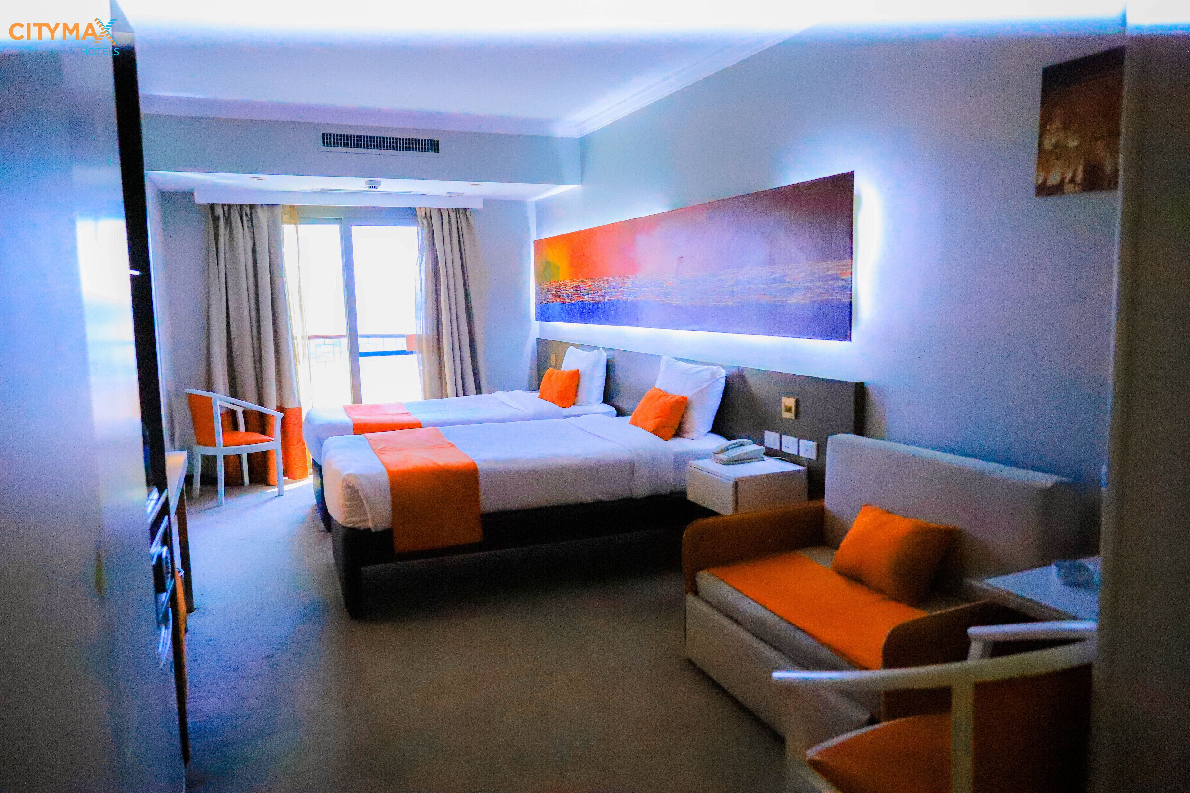 Ett hotellrum med två sängar, en soffa, en fåtölj och en stor tavla på väggen.