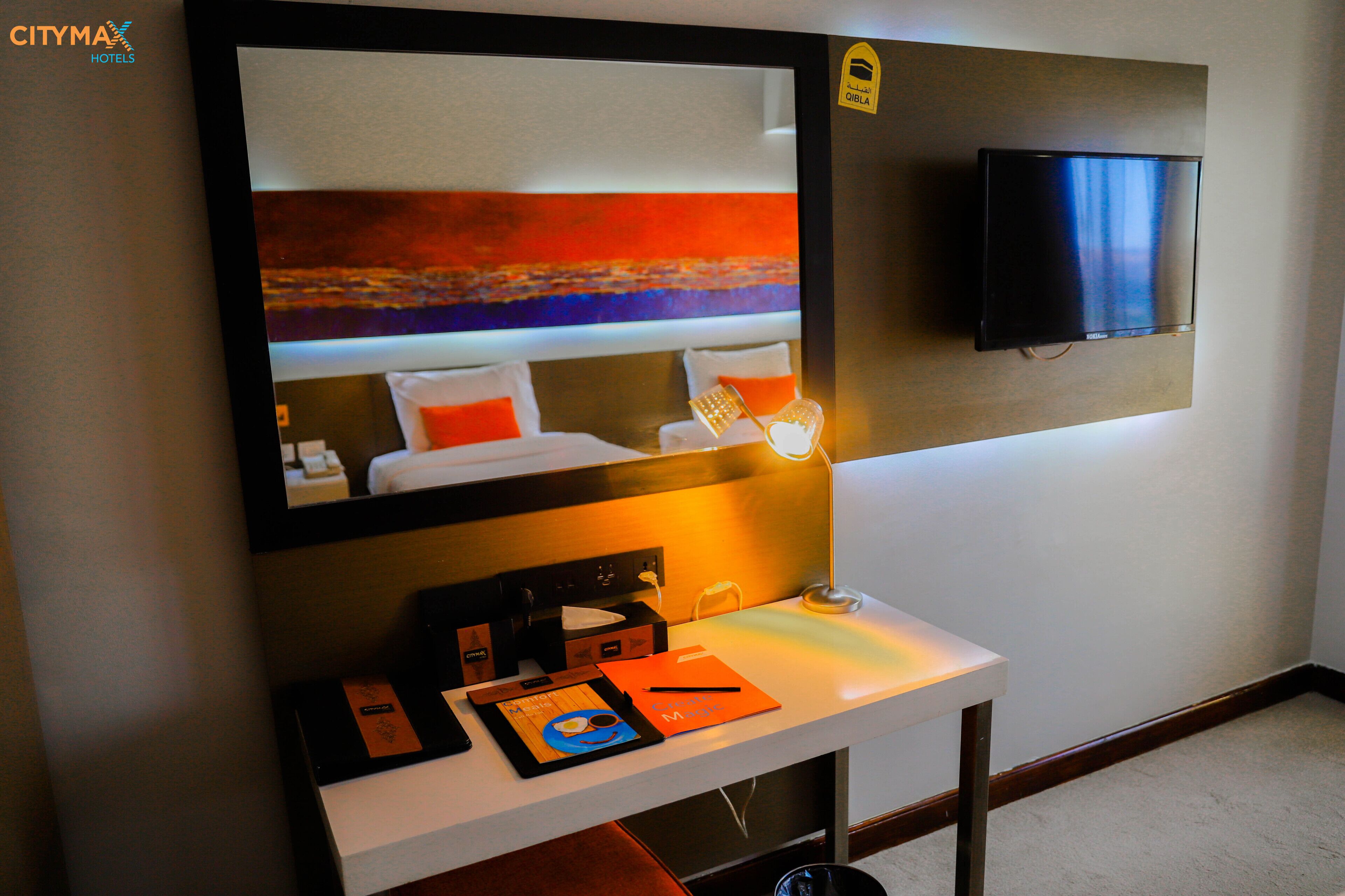 Habitación de hotel con un espejo grande, un televisor de pantalla plana, una mesita de noche con lámpara y vista al mar.