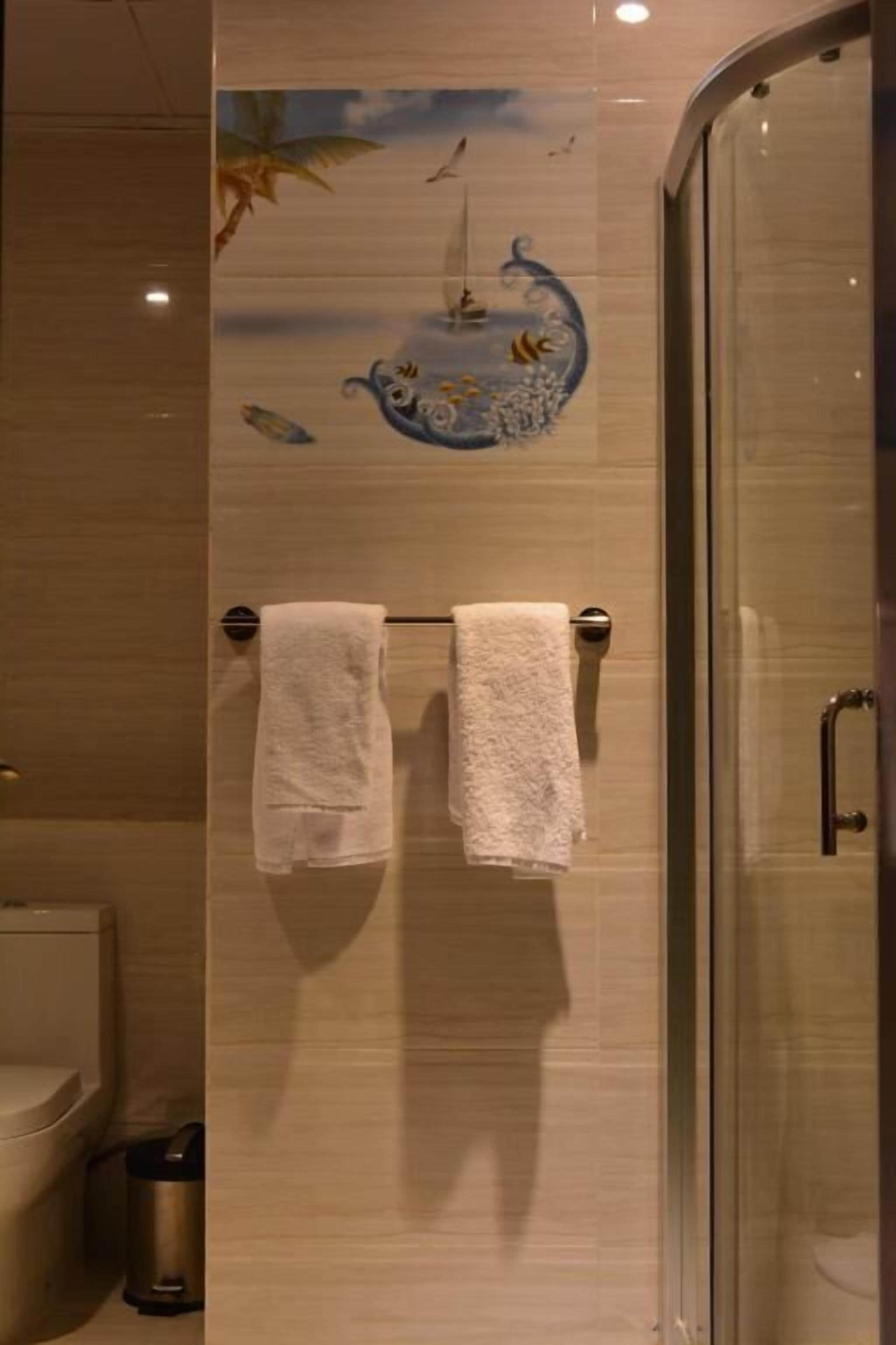 A bathroom with a glass shower door, two white towels hanging on a towel rack, and a decorative wall mural.