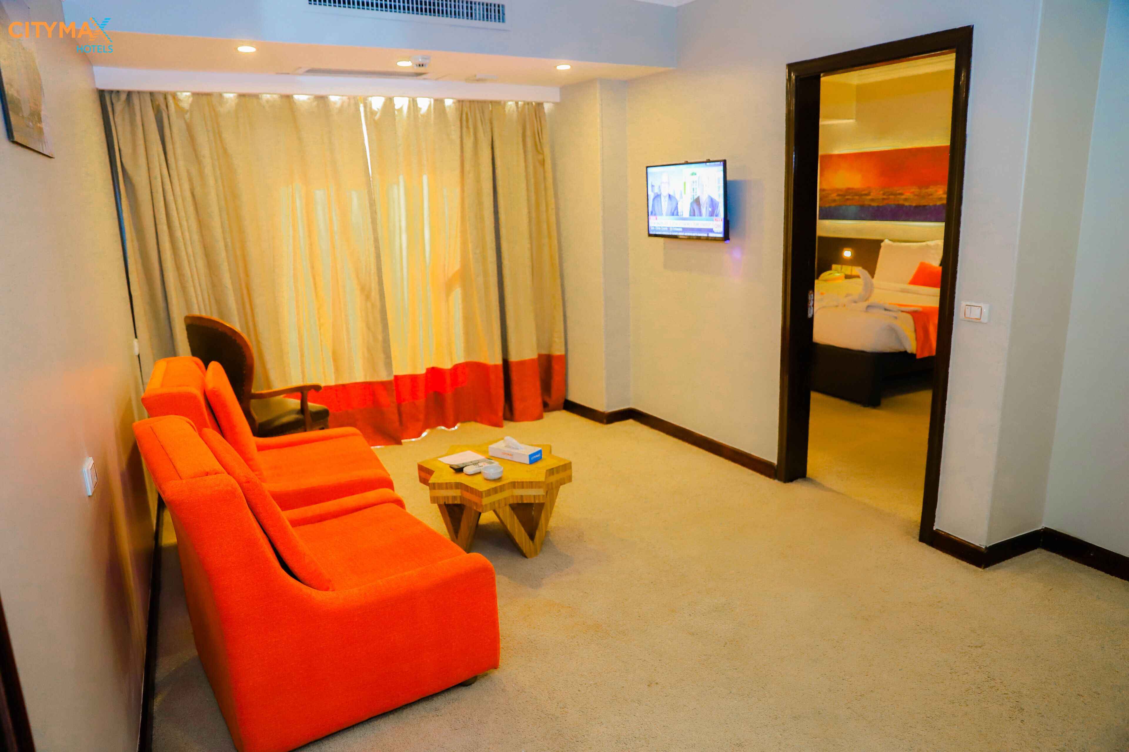 A hotel room with a large orange sofa, a small wooden table, and a television on the wall.