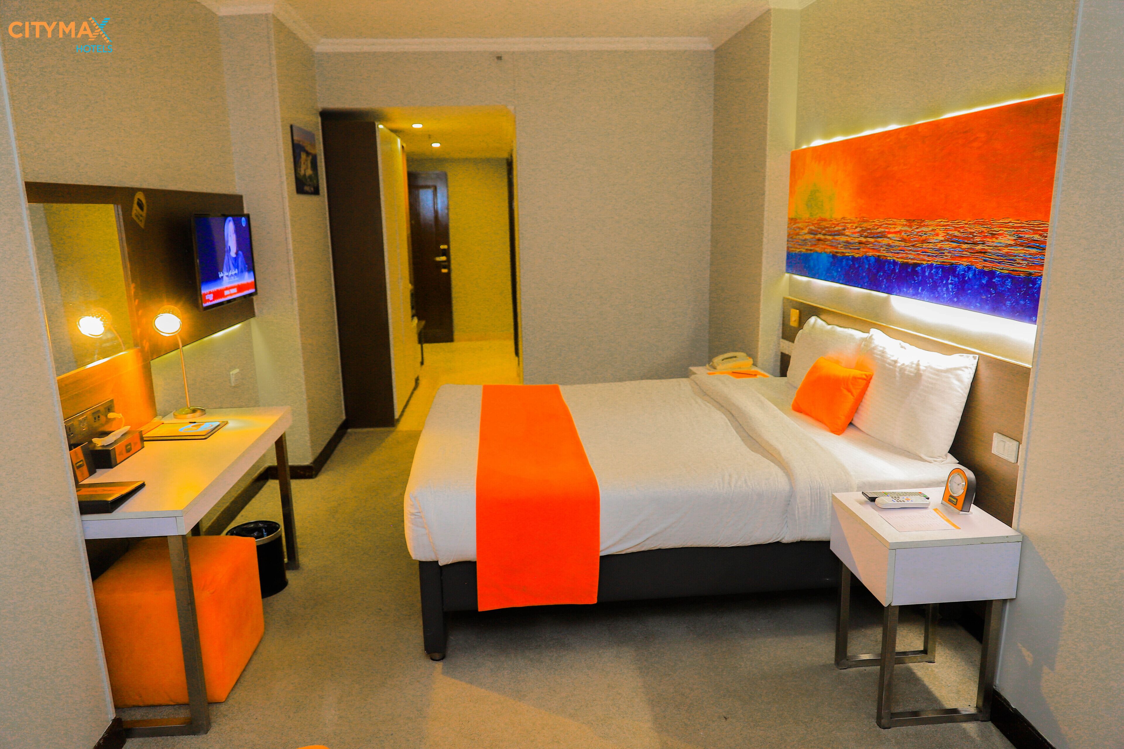 Una habitación de hotel con cama, escritorio, televisor y un cuadro en la pared.