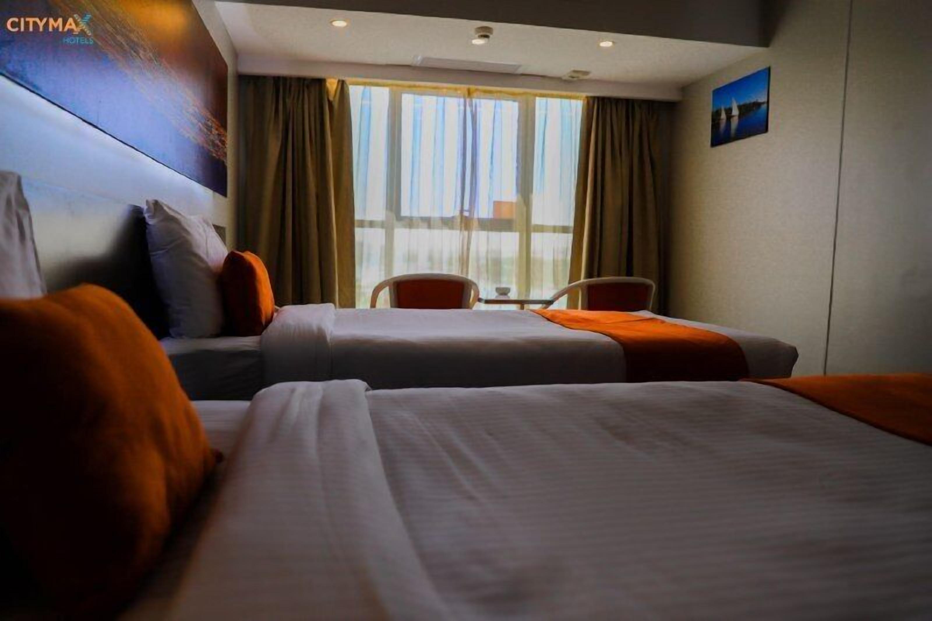 Habitació d'hotel amb dos llits, una finestra gran amb cortines, una cadira i una taula.