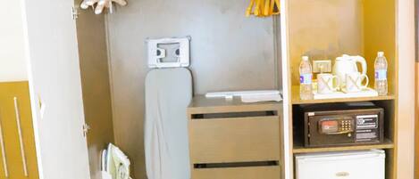 A compact hotel room with a wardrobe, a small refrigerator, a microwave, and a shelf with toiletries.